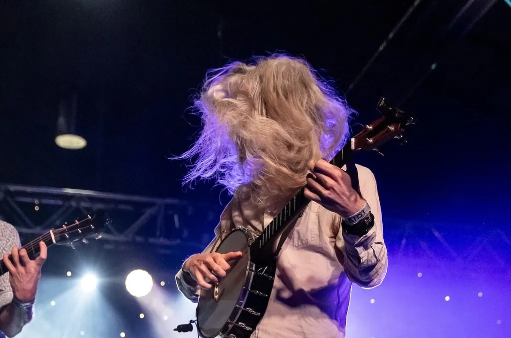 Nick Henderson mid-headbang at the banjo, long hair flying in blue and violet light